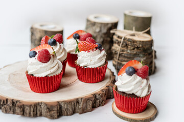 red cream cupcakes with strawberries and blueberries on natural wood coasters