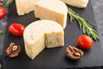 Cheddar cheese and various types of cheese with rosemary and tomatoes on black slate board on a black concrete background. Side view, selective focus.