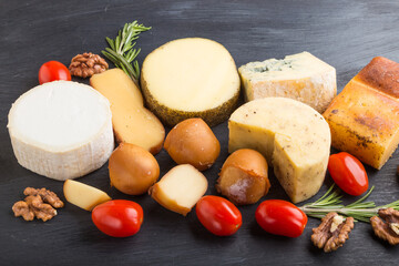 Set of different types of cheese with rosemary and tomatoes on a black wooden background. Side view.
