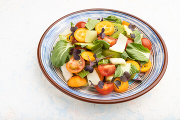 Vegetarian salad of pac choi cabbage, kiwi, tomatoes, kumquat on a white concrete background. Side view, close up.