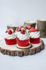 red cupcakes with cream and fresh fruit served on natural raw wood slices and coasters table setting 