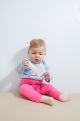 A little girl, eight months old, is sitting on the couch holding an ear piercing device. Beauty for young children