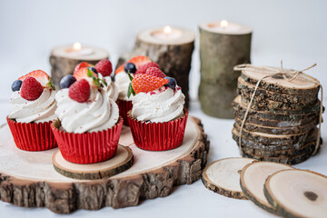 red cream cupcakes with strawberries and blueberries on natural wood coasters