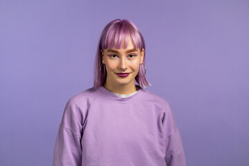 Portrait of trendy woman over violet studio background. Positive young girl with dyed purple hair smiles to camera.