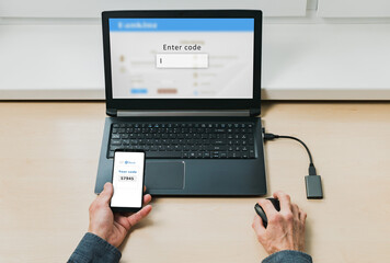 An adult male works with a computer and a cell phone