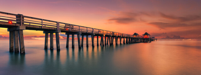 Fototapeta premium Panoramic shot of a scenic colorful sunset at the beach with breathtaking boardwalk