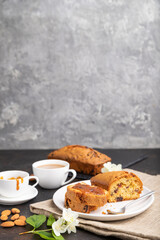 Fototapeta na wymiar Homemade cake with raisins, almonds, soft caramel and a cup of coffee on a black concrete background. Side view, copy space, selective focus.