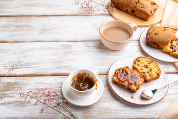 Homemade cake with raisins, almonds, soft caramel and a cup of coffee on a white wooden background. Side view, copy space.