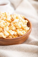 Popcorn with caramel in wooden bowl and a cup of coffee on a white wooden background. Side view, selective focus.