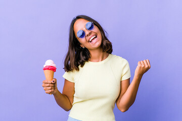 Young mixed race woman eating an ice cream raising fist after a victory, winner concept.