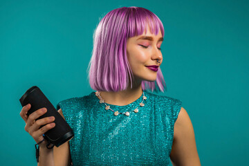 Unusual woman with dyed violet hairstyle listening to music by wireless portable speaker - modern...