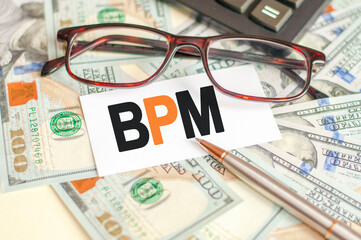 the letters BPM are written on a white card lying on the bills, glasses, pen and calculator in the background, concept of business and finance