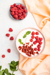 Yogurt with raspberry and goji berries in ceramic bowl on white concrete background. top view.