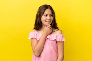 Little caucasian girl isolated on yellow background looking to the side and smiling