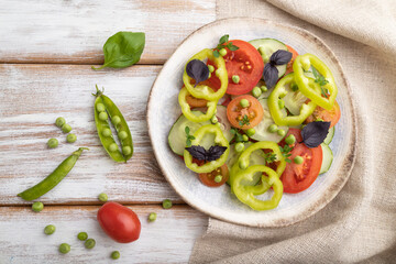 Vegetarian salad from green pea, tomatoes, pepper and basil on white wooden background. top view, close up.