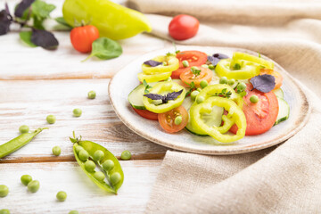 Vegetarian salad from green pea, tomatoes, pepper and basil on white wooden background. Side view, selective focus.