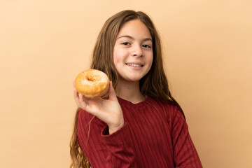 Little caucasian girl isolated on beige background holding a donut and happy