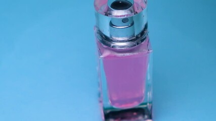 Close-up. Water flows on a faceted bottle with a transparent lid and pink perfume on a blue background and creates waves - Powered by Adobe