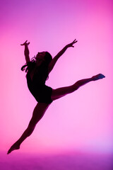Professional ballerina dancing ballet in spotlights smoke. Beautiful young female wearing black bodysuit on floodlights background.