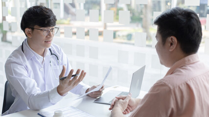 Young Asian man in a white robe talks to a man, Doctors diagnose diseases and give advice or treatment solutions to patients in the hospital examination room, Explaining medical examination results.