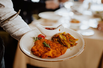 Waiter holding Viennese Schnitzel with fried potatoes, rosemary and ketchup