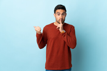 Young handsome man over isolated background pointing to the side and doing silence gesture
