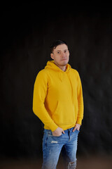 Portrait of young man on black background. Handsome guy in yellow hoodie posing on dark background.