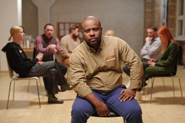 Bald serious man of African ethnicity looking at you against patients of mental support group