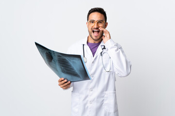 Young doctor man holding a radiography isolated on white background shouting with mouth wide open