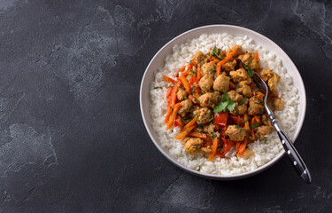 Vegan stew soy meat and vegetables served with boiled rice and greens on black textured background. delicious healthy diet food. space, top view
