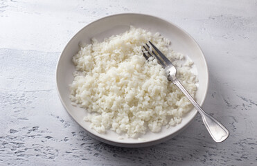 Bowl of cooked white rice on light gray textured background, selective focus, top view, horizontal