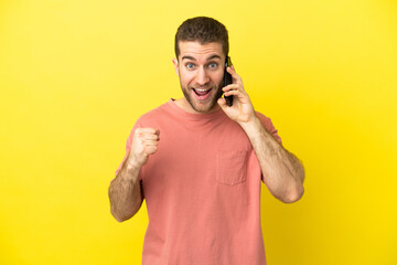 Handsome blonde man using mobile phone over isolated background celebrating a victory in winner...