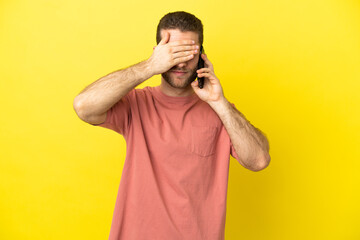 Handsome blonde man using mobile phone over isolated background covering eyes by hands. Do not want to see something