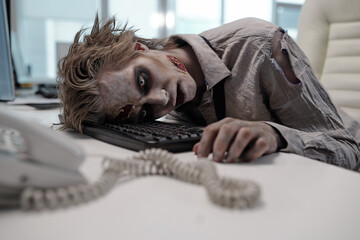 Dead businessman with zombie body painting keeping head on computer keyboard after working - obrazy, fototapety, plakaty