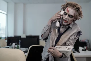 Fotobehang Zombie businessman with phone receiver by ear standing by workplace in front of camera © pressmaster