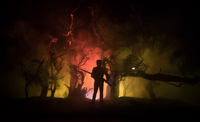 Man with riffle against zombie attack. Zombie apocalypse. Scary view of blurred zombies at cemetery and spooky cloudy sky with fog. Horror Halloween concept.