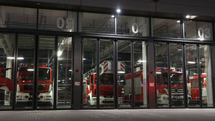 Fire station view at night with fire trucks parked in front of the gates ready to be deployed if...