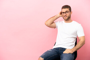 Fototapeta premium Young man sitting on a chair over isolated pink background having doubts