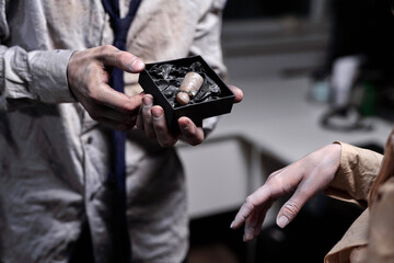Hand of dead businessman holding small box containing cut finger with engagement diamond ring