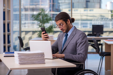 Obraz premium Young male employee in wheel-chair working in the office