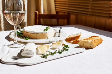 Delicious cheese brie or camembert, baguette and glass of wine on the table with white tablecloth. Dairy products. Italian, French cheese. Breakfast.