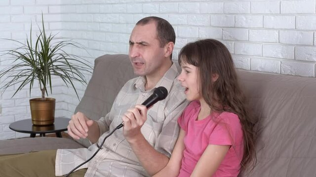 The cheerful family is singing. Father and his teenage daughter sing karaoke at home.