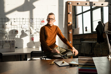 Young serious tailor with prosthesis instead of left leg sitting by workplace in front of camera