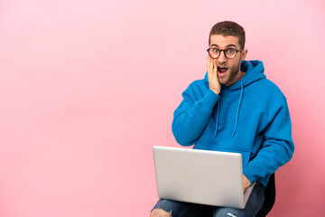 Young man sitting on a chair with laptop with surprise and shocked facial expression