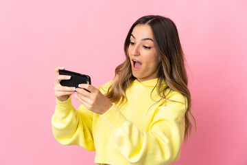 Young Romanian woman isolated on pink background playing with the mobile phone