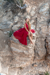 A girl with loose hair in a red dress sits on a rock rock above the sea. In the background, the sea. The concept of travel.