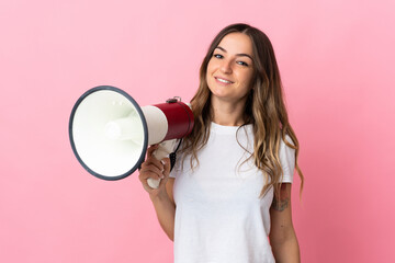 Young Romanian woman isolated on pink background holding a megaphone and smiling a lot