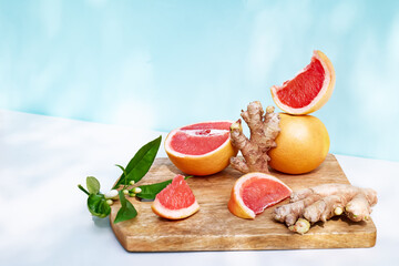 Fresh healthy grapefruit and ginger on sunlight with shadows. Minimal food creative concept on blue pastel background. Grapefruit slices citrus fruits
