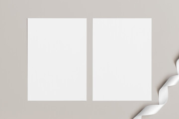 Two white invitation cards mockup with a satin tape decoration on the beige table. 5x7 ratio, similar to A6, A5.