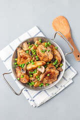 Chicken with potatoes, mushrooms and green peas, in metal pot, vertical, top view